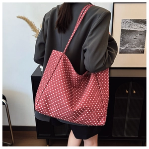 Detail shot of a large red polka dot canvas tote bag worn on a shoulder over a grey blazer
