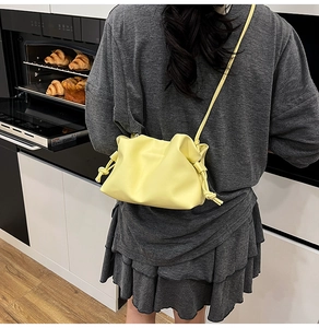 Detail of a lemon yellow pleated cloud bag worn as a shoulder bag in a casual setting