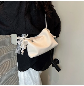 Chic beige shoulder bag featuring pearl charms and lace bow detailing worn by a model