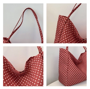 Detail view of red canvas tote bag with white polka dots and reinforced stitching