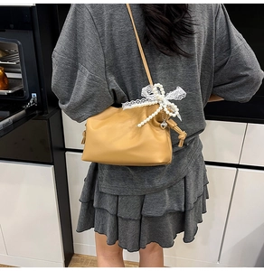Detail of khaki cloud bag featuring oversized lace bow and elegant pearl charm accent