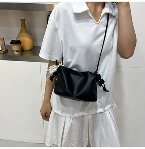 Detail of black crossbody bag with drawstring knot and decorative pearl tassel accessory