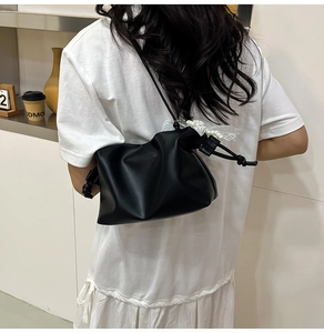 Close-up of black pleated cloud bag with pearl and lace charm on a model's shoulder