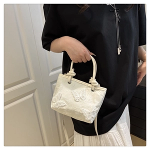 Détail d'un sac à main en dentelle blanche avec broderies papillon 3D et poignée tressée