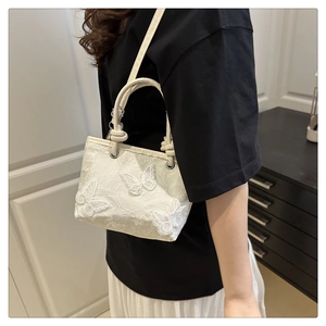 Détail du sac seau blanc avec broderie papillon complexe et poignée tressée élégante