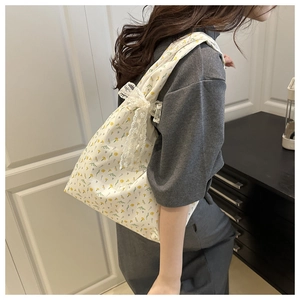 Detail of floral canvas tote bag featuring yellow flower patterns and lace bow accessory