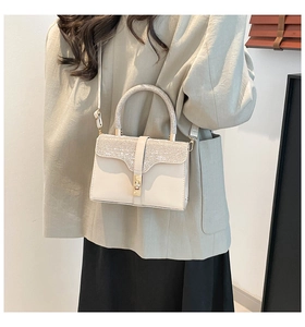 Detail of cream crossbody bag featuring a sparkling rhinestone-encrusted handle and golden lock