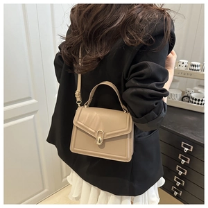 Detail of beige structured handbag with gold oval twist lock and adjustable shoulder strap