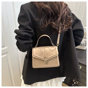 Beige flap crossbody bag with gold buckle worn over a black blazer and white pleated skirt