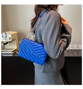 Detail of royal blue quilted handbag with silver chain strap on a model in a cafe