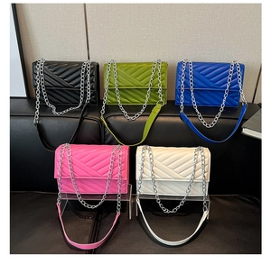 Five colors of V-quilted flap bags with silver chain straps displayed on a leather sofa