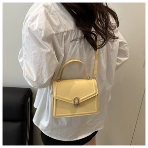 Detail of cream yellow crossbody bag with metal U-shaped clasp shown on a model