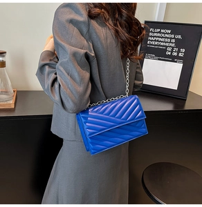 Detail view of blue V-quilted chain handbag worn over a dark grey blazer jacket