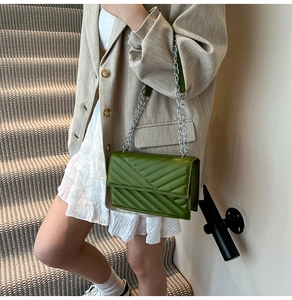 Detail of dark green quilted shoulder bag with V-shaped stitching and silver chain strap