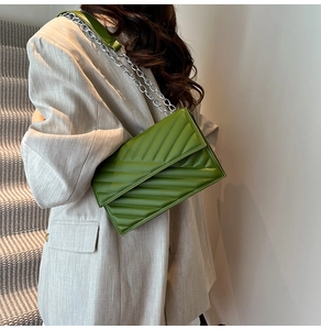 Detail of green quilted crossbody bag with silver chain strap on light blazer