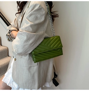 Detail of green chevron quilted shoulder bag with silver chain strap on model