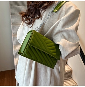 Detail of bright green V-quilted faux leather bag with silver chain strap on a model