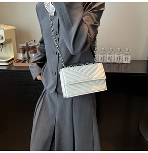 White quilted chain shoulder bag with diamond pattern shown on model in a cafe setting