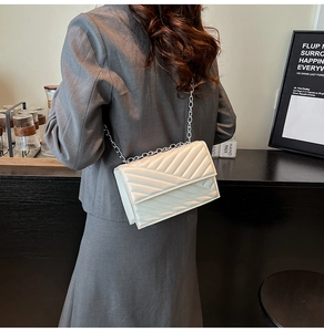 Modern creamy white quilted chain bag worn by model in a stylish interior setting