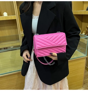 Detail of rose red quilted leather envelope bag with silver chain strap on model