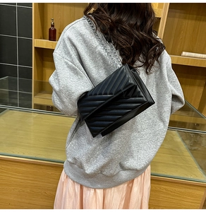 Side view of black quilted envelope bag with silver chain strap on a female model