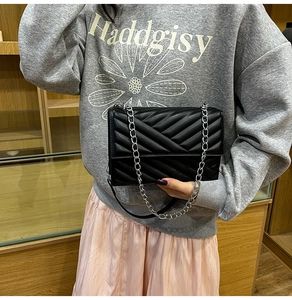 Close-up of black V-quilted leather handbag with silver chain strap worn by a model