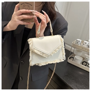 Detail of off-white faux leather mini bag featuring decorative fringe and metal chain strap