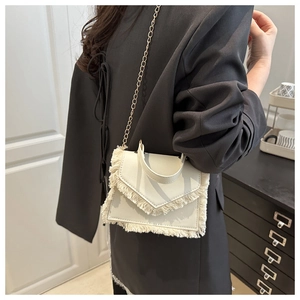 Detail of off-white mini square bag with fringe edges and gold chain strap on grey blazer