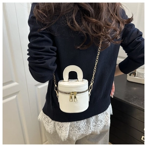 Détail du sac seau cylindrique en cuir blanc avec bandoulière dorée sur un mannequin