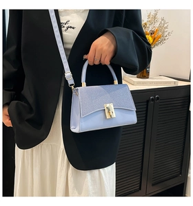 Detail of light blue crossbody bag with woven texture flap and gold metallic hardware