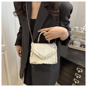Detailed view of white envelope-style bag with fringe trim and golden chain strap
