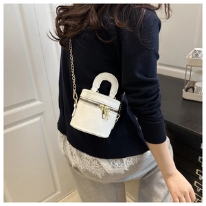 Détail du mini sac cylindrique blanc avec bandoulière chaîne dorée porté par un mannequin