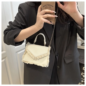 Detail showing cream white mini crossbody bag with elegant fringe edge and gold chain strap
