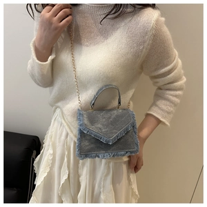 Detail view of denim crossbody bag with fringe edges and gold chain strap on model