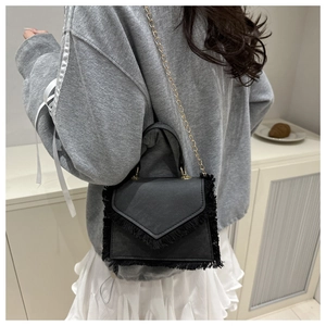 Detailed view of a black fringe crossbody bag with gold chain and V-shaped flap cover