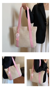 Close-up of straw woven tote bag with pink canvas straps and a cute plush charm
