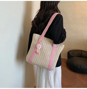 Detail of woven straw tote bag with pink straps and plush charm worn by model