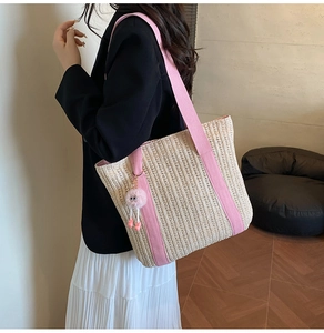 Detail of woven straw tote bag with pink vertical straps and cute fuzzy eye charm