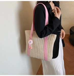 Detail of straw tote bag with pink woven straps and cute plush charm on a model