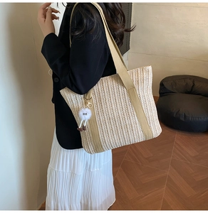 Detail of hand-woven straw tote bag featuring a beige shoulder strap and plush charm