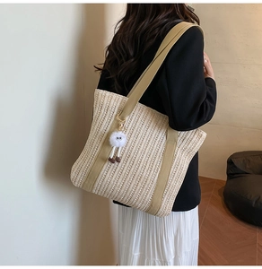Detail of a beige woven straw tote bag with khaki canvas straps and a white plush pompom charm