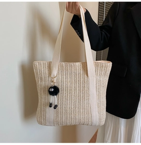 Detail of a beige woven straw tote bag with black soot sprite plush charm and canvas straps