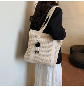 Close-up of beige woven straw tote bag with white fabric strap and fuzzy charm