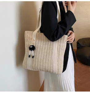 Detail of beige straw tote bag featuring white canvas strap and black soot sprite charm