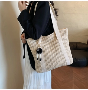 Detail of woven straw tote bag featuring white handles and a black plush ball charm