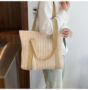 Detail of woven straw tote bag featuring a decorative tassel and wide canvas shoulder strap