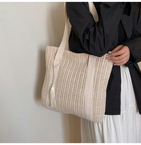 Detail of beige woven tote bag with vertical textures and smooth tassel charm for summer