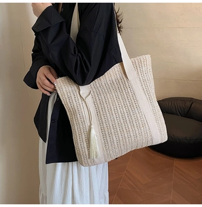 Detail of beige woven straw tote bag featuring a decorative tassel and wide shoulder strap