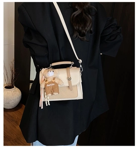 Detail of cream and brown crossbody bag with metal twist lock and cute plush bear charm