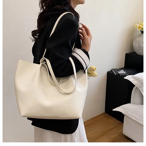 Minimalist creamy white leather tote bag shown on shoulder in a modern home setting